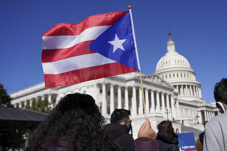 A woman waves a Puerto Rican flag. The Capitol building is visible in the background.