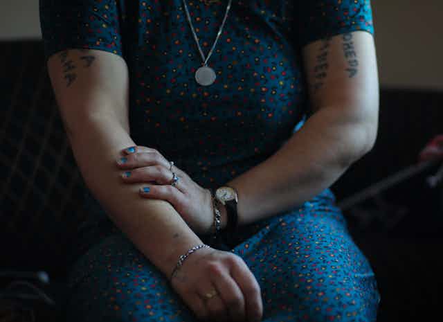 Cropped image of a woman in a blue dress with tattoos on her arms