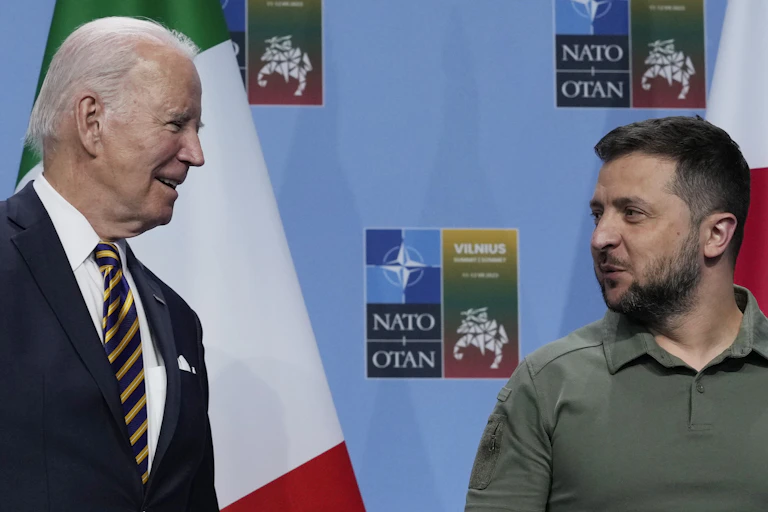 Two men, one in a suit and tie the other in a green shirt chat to each other.
