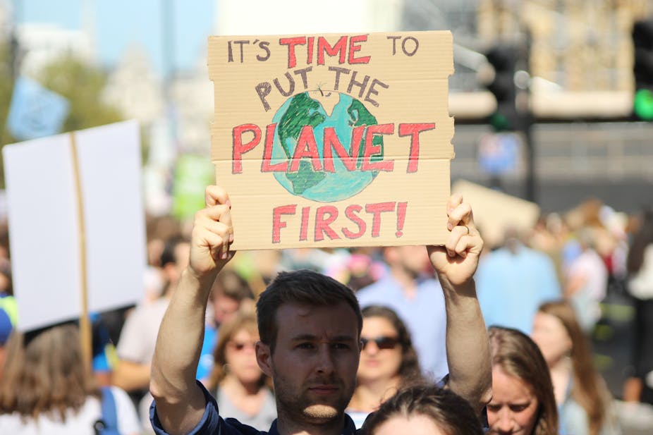Un homme tient une pancarte sur laquelle on peut lire « Il est temps de mettre la planète au premier plan » lors d’un rassemblement climat 