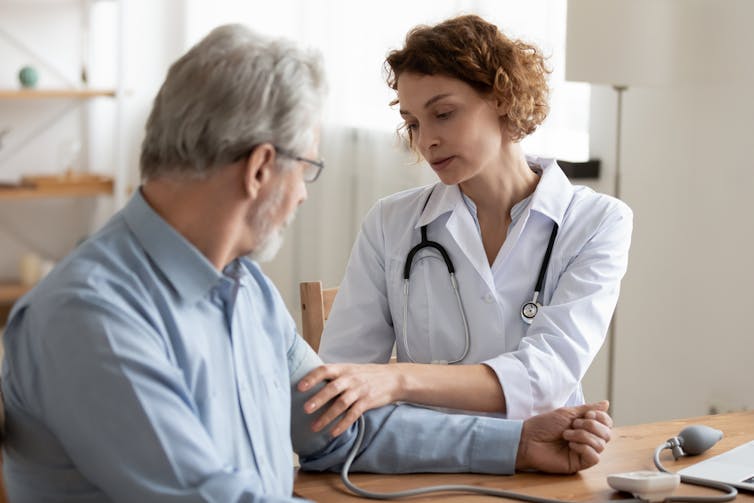 Female doctor checking blood pressure of older male