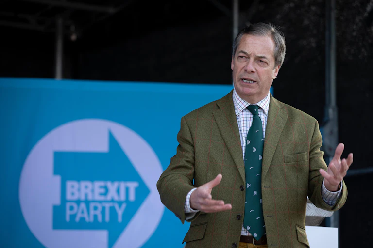 Nigel Farage giving a speech in front of a Brexit Party sign.