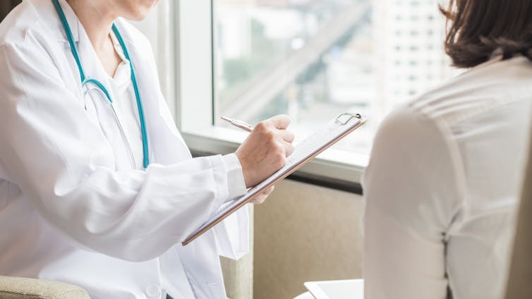 A doctor writes on a clipboard while speaking with a patient.