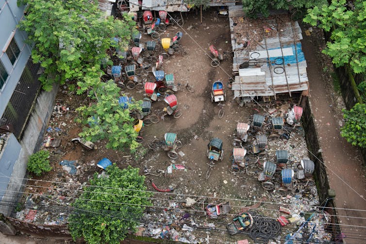 Cycle-rickshaws parked in an empty city lot, seen from overhead.