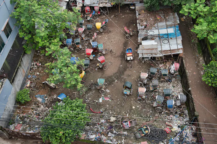 Cycle-rickshaws parked in an empty city lot, seen from overhead.