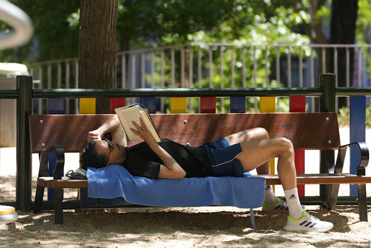 A man reading while lying on bench.