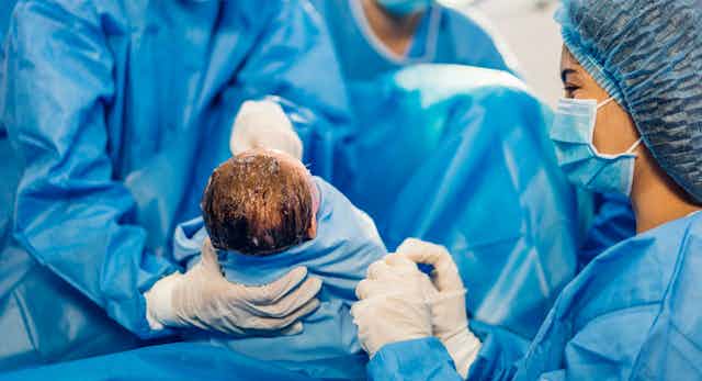 Un equipo médico sostiene a un bebé envuelto en un material azul.