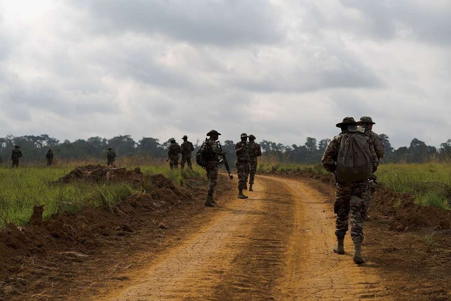 Armed soldiers on foot patrolling a dusty rural road