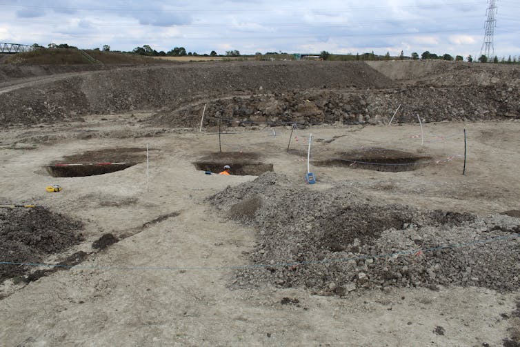 Three pits in alignment on a muddy strip of land.