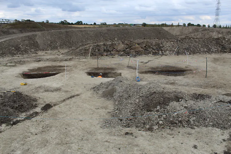 Three pits in alignment on a muddy strip of land.