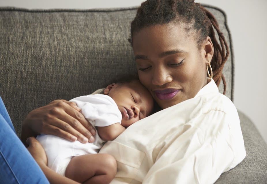 A young mother with eyes closed holds a sleeping infant on her chest.