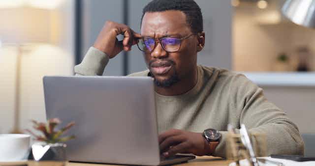 a man wearing glasses looks at a laptop screen with a puzzled expression