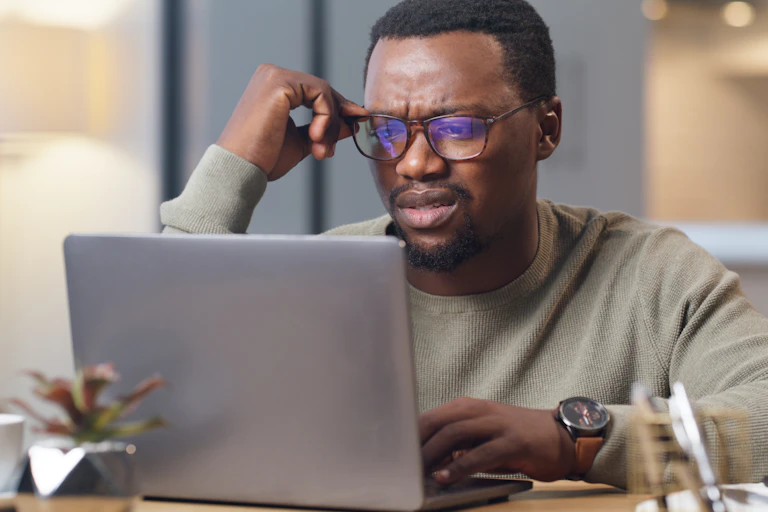 a man wearing glasses looks at a laptop screen with a puzzled expression
