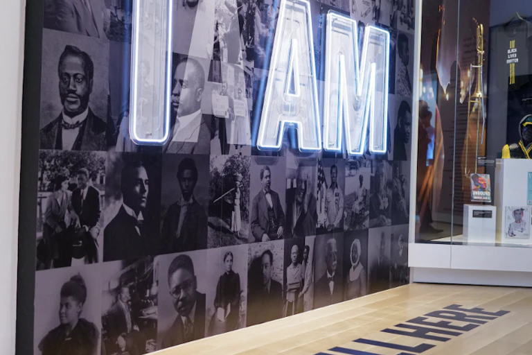 The white letters "I Am" are seen over a background of photographs of Black people.