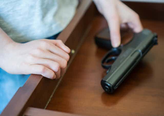 child's hands reach for a handgun in a drawer