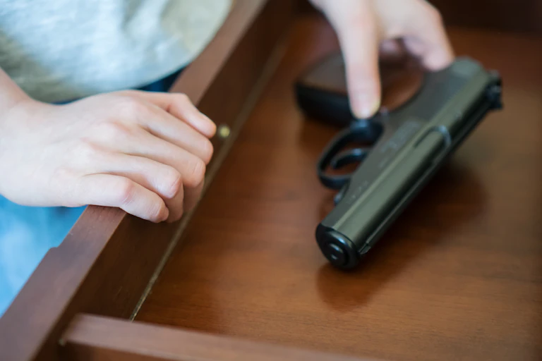 child's hands reach for a handgun in a drawer