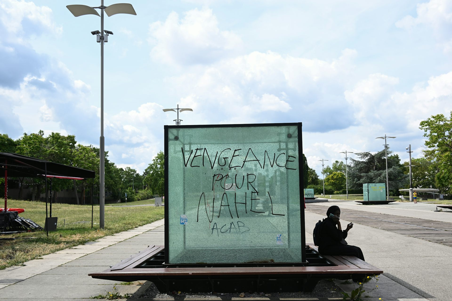 Une personne consulte son smartphone à côté d'une vitre portant l'inscription « Vengeance pour Nahel. ACAB »