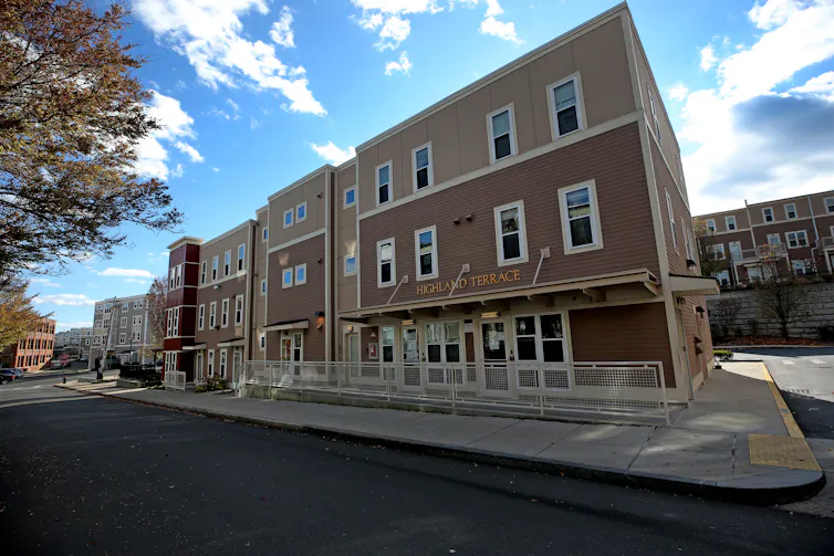 A row of apartments that look like townhouses lines a street. A similar row is on the hill behind them.
