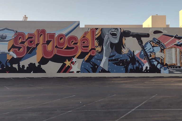 A mural reads "san jose!" and shows a woman singing into a microphone. In the foreground is a large empty parking lot.