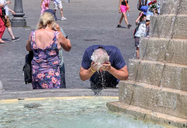 A tourist refreshes his head with water from a fountain on a very hot day.