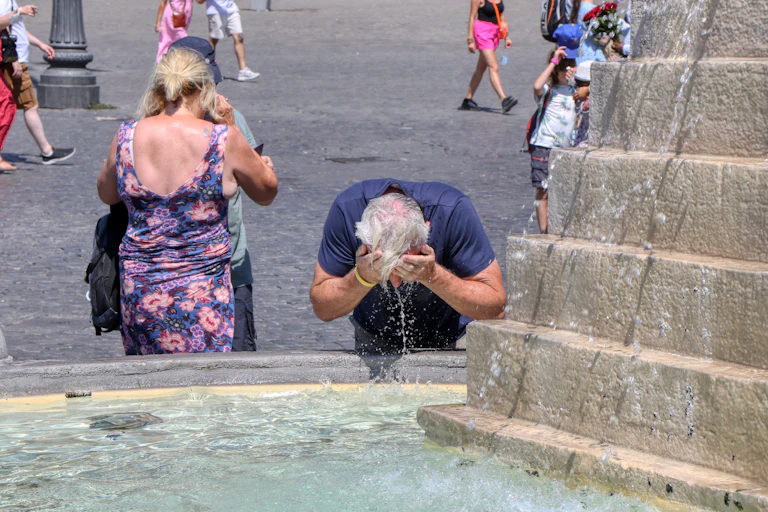 A tourist refreshes his head with water from a fountain on a very hot day.