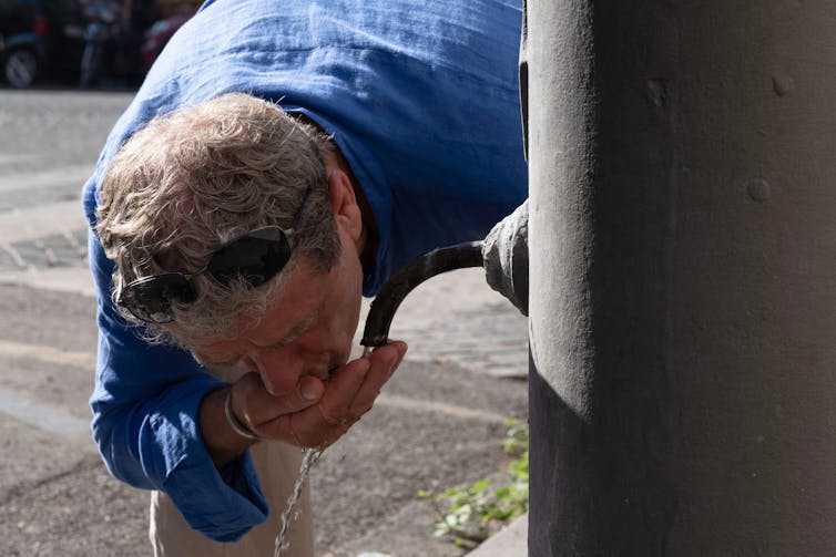 A man drinking water from a public water fountain.