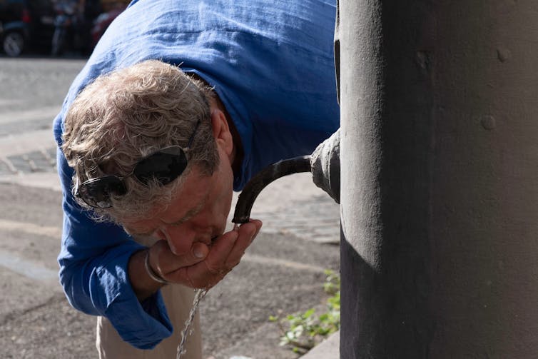 Un hombre bebe agua de una fuente pública. calor