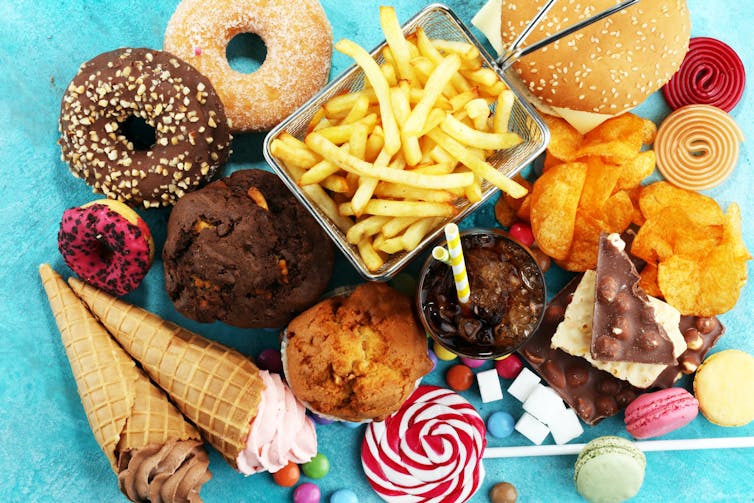 A selection of food, including chips, doughnuts, ice cream and cakes are laid out on a blue table.