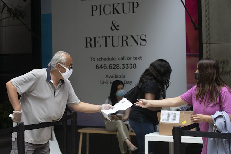 A man hands a slip of paper to a woman a returns desk at Saks Fifth Avenue.