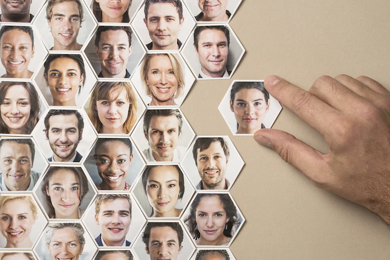 A grid of hexagons, each containing a headshot of a different face. A hand removes one hexagon from the grid.