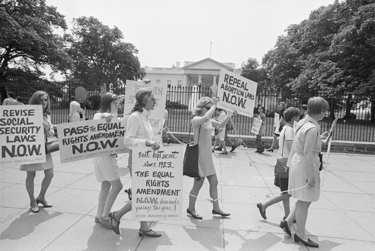 A black and white photo shows women marching and holding signs that say 'Pass the equal rights amendment NOW'