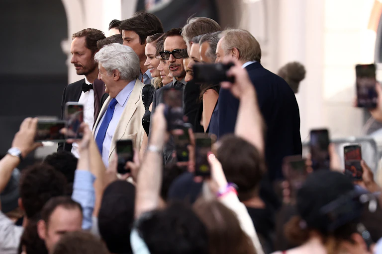 A groups of men and women stand on a platform while cameras are held aloft in front of them.