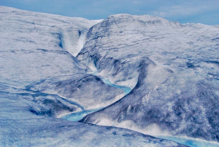 Meltwater pours over the Greenland ice sheet in a meandering channel.