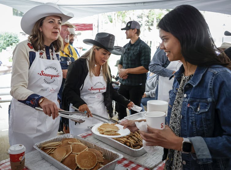 A woman in a cowboy hat serves pancakes to a dark-haired woman.