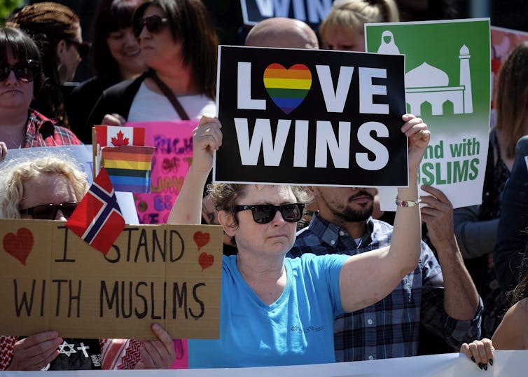 A person in a blue T-shirt holds up a sign that reads Love Wins at an anti-racism protest.