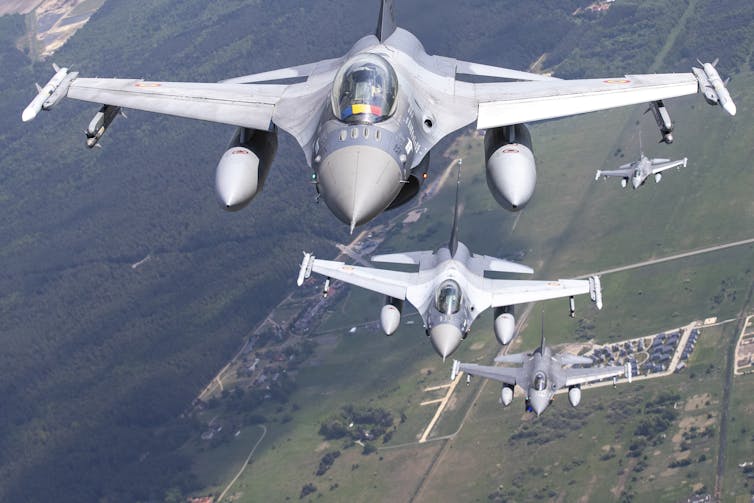 Fighter jets fly in formation over green countryside and forest.