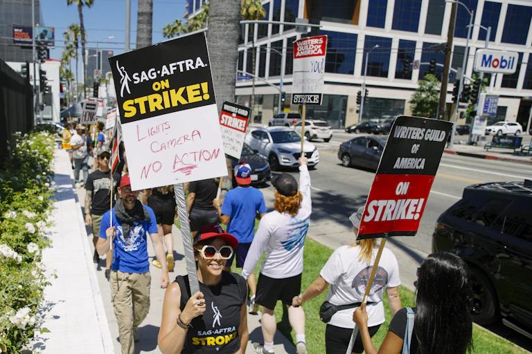 People in sunglasses march carrying signs saying they're on strike