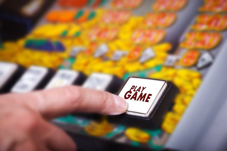 Finger pressing play button on pokie machine