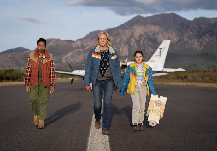 A woman and two children walk on a tarmac.