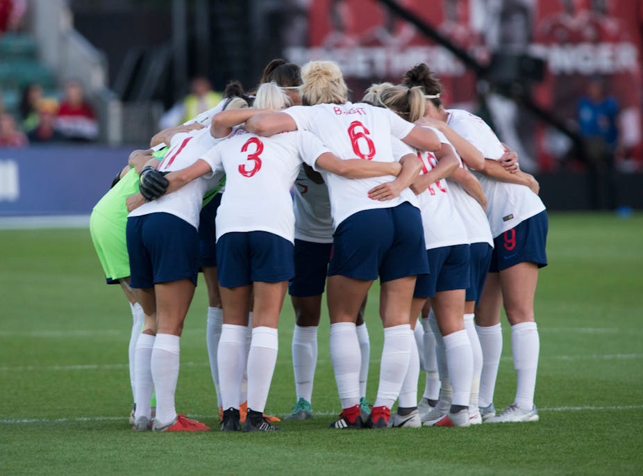 The England women's team huddle on the pitch. 