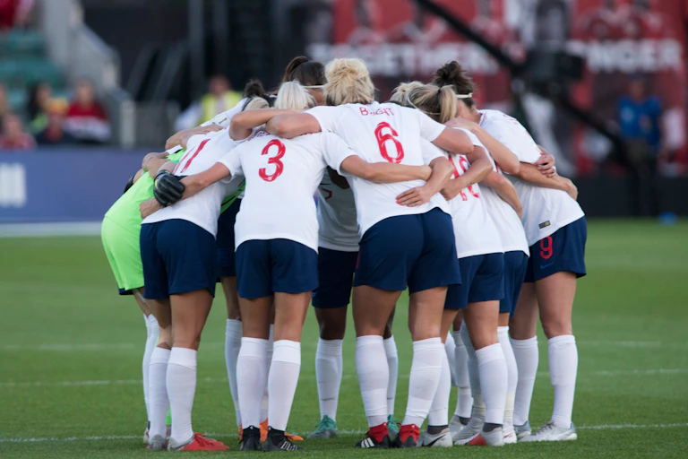 The England women's team huddle on the pitch.