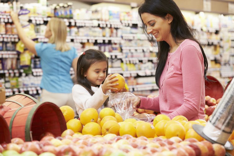 A parent and child in the fruit section of grocery store.