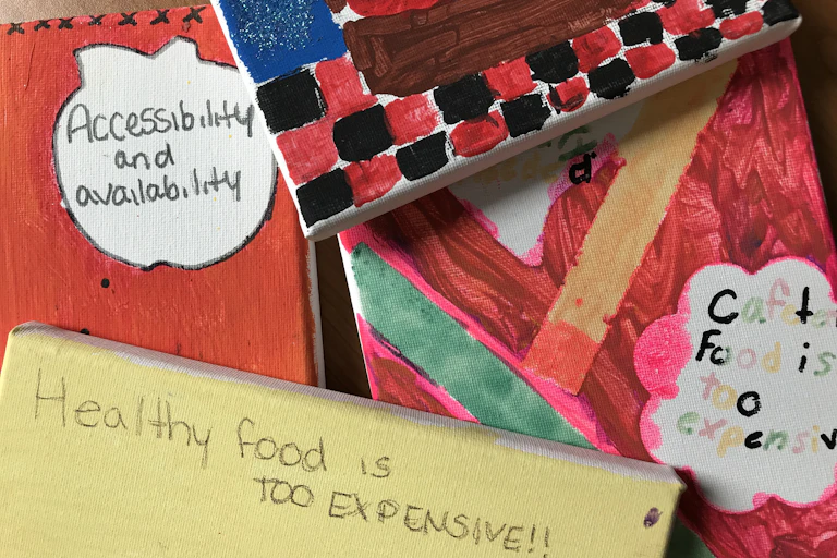 Schoolchildren's artwork on canvas. One says 'healthy food is too expensive'