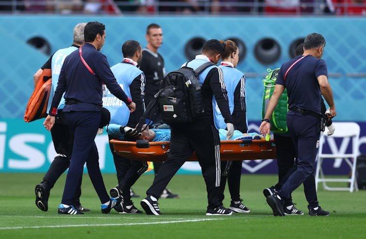 Medical staff carrying man on stretcher off football pitch