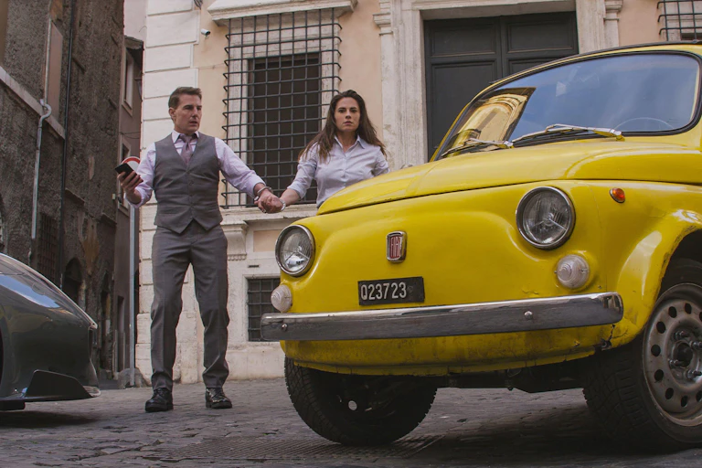 Two people hold hands and look at an old car.