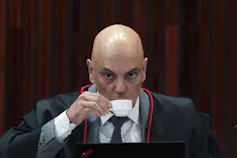 A bald man sips from a white cup.