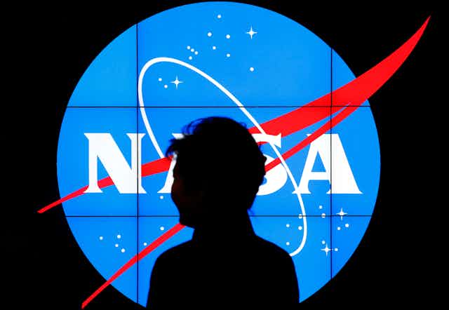 A man stands silhouetted in front of a bright NASA logo
