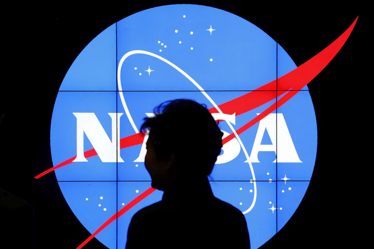A man stands silhouetted in front of a bright NASA logo