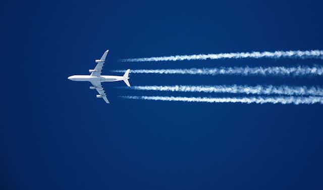 white jet flying with four contrail streams against bright blue sky