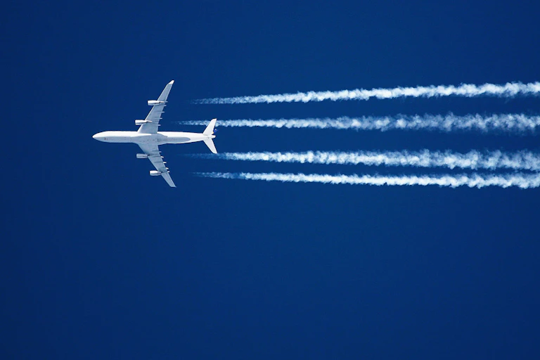 white jet flying with four contrail streams against bright blue sky